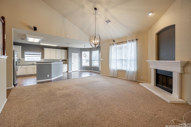 unfurnished living room featuring light carpet, sink, high vaulted ceiling, and an inviting chandelier