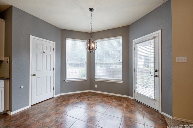 unfurnished dining area featuring an inviting chandelier, plenty of natural light, and dark tile patterned floors