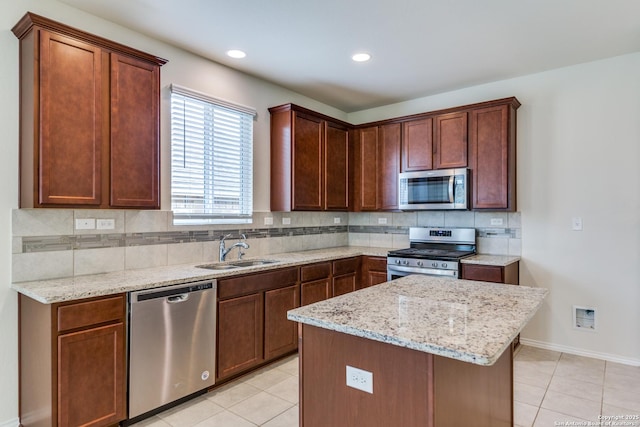 kitchen featuring backsplash, a kitchen island, sink, light stone countertops, and appliances with stainless steel finishes