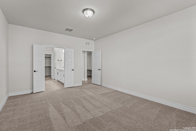 unfurnished bedroom with ensuite bathroom, light colored carpet, and a textured ceiling