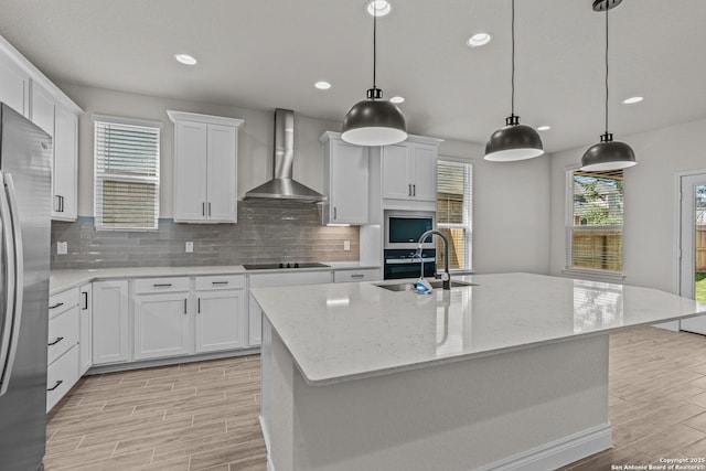 kitchen featuring sink, wall chimney range hood, and a center island with sink