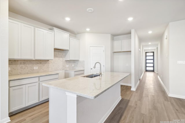 kitchen featuring a kitchen island with sink, white cabinets, light stone counters, and sink