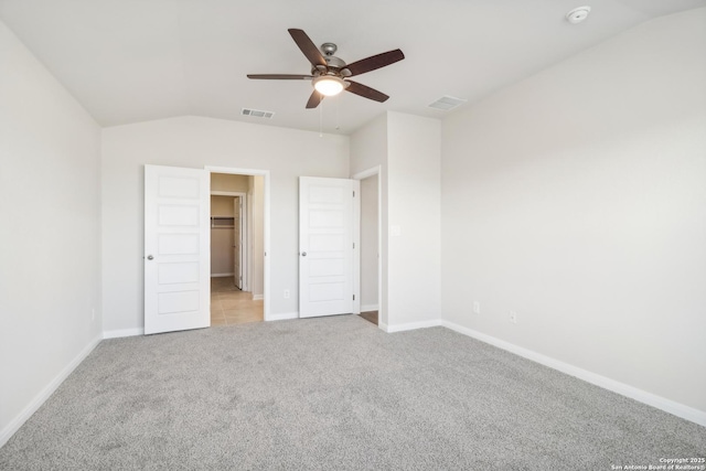 unfurnished bedroom featuring a spacious closet, light carpet, ceiling fan, a closet, and lofted ceiling