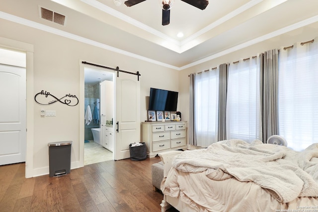 bedroom with a barn door, hardwood / wood-style floors, ceiling fan, ensuite bath, and crown molding