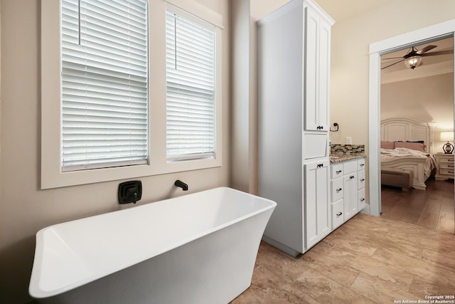 bathroom featuring ceiling fan, vanity, backsplash, a tub to relax in, and ornamental molding