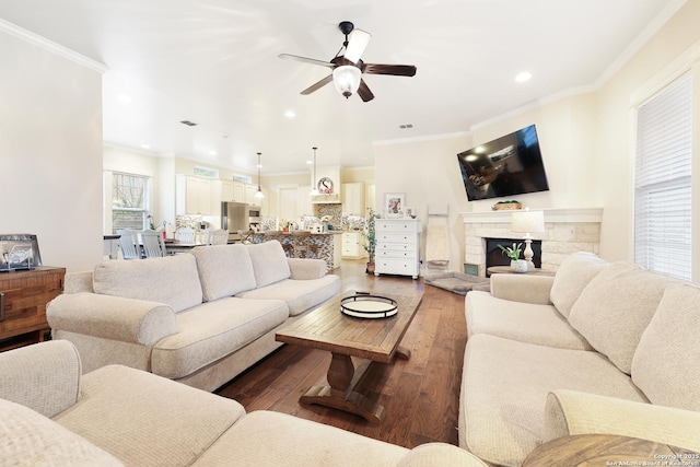 living room with ceiling fan, dark wood-type flooring, a stone fireplace, and ornamental molding