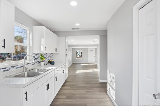 kitchen with light wood-type flooring, decorative backsplash, white cabinets, and sink