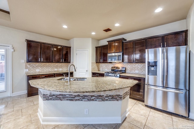 kitchen featuring light stone countertops, sink, appliances with stainless steel finishes, and an island with sink