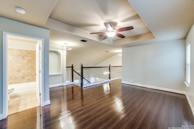 spare room featuring dark wood-type flooring, a tray ceiling, and ceiling fan