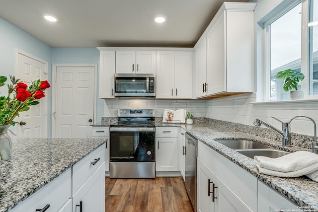 kitchen with white cabinets, appliances with stainless steel finishes, sink, backsplash, and light wood-type flooring