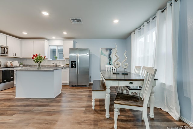 kitchen featuring white cabinetry, stainless steel appliances, decorative backsplash, stone countertops, and hardwood / wood-style flooring