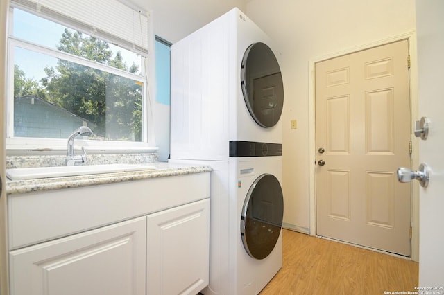 clothes washing area featuring cabinets, sink, stacked washing maching and dryer, and light wood-type flooring