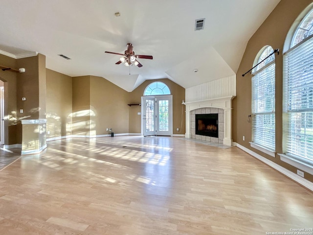 unfurnished living room with ceiling fan, vaulted ceiling, a tiled fireplace, and light wood-type flooring