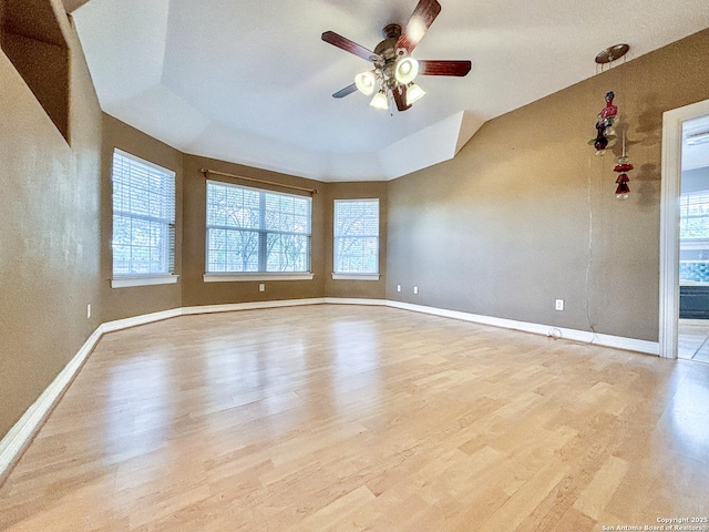 spare room with ceiling fan, vaulted ceiling, a tray ceiling, and light hardwood / wood-style flooring