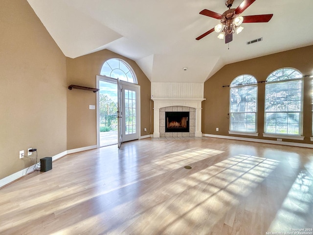 unfurnished living room with ceiling fan, a tiled fireplace, plenty of natural light, and light hardwood / wood-style floors