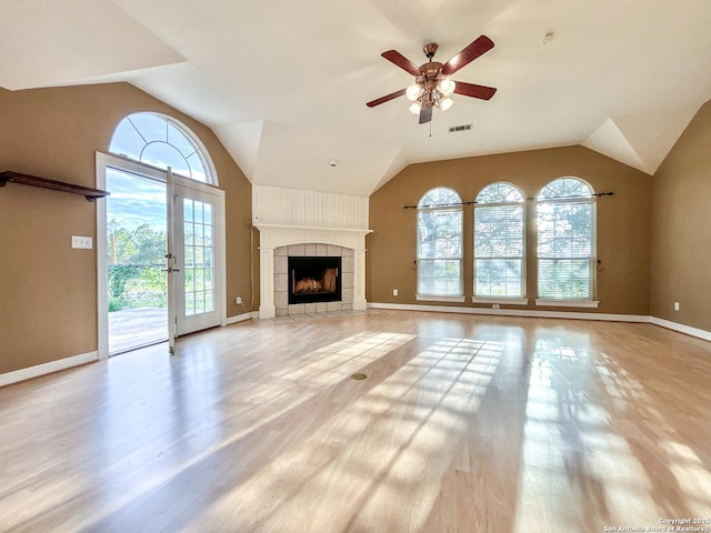 unfurnished living room featuring lofted ceiling, french doors, a fireplace, ceiling fan, and light hardwood / wood-style flooring