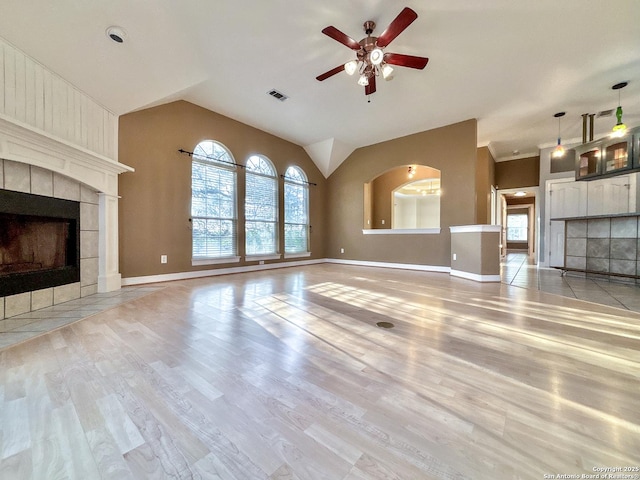 unfurnished living room with light hardwood / wood-style floors, a tile fireplace, ceiling fan, and vaulted ceiling