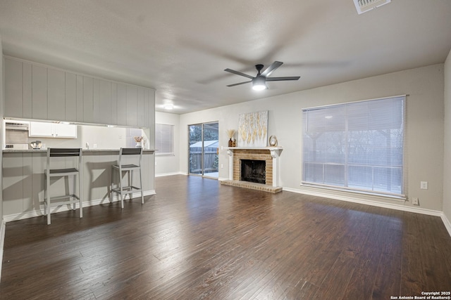 unfurnished living room featuring ceiling fan, dark hardwood / wood-style flooring, and a brick fireplace