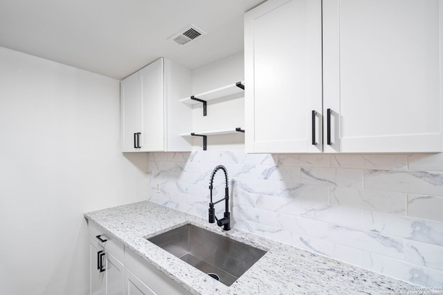 kitchen with white cabinetry, backsplash, light stone counters, and sink