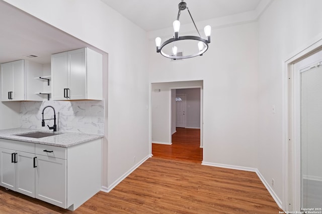 kitchen with white cabinets, tasteful backsplash, light hardwood / wood-style floors, sink, and a chandelier