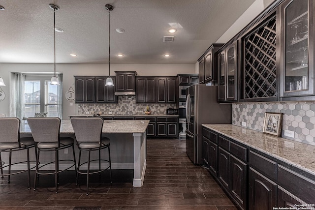 kitchen with stainless steel refrigerator, tasteful backsplash, dark brown cabinetry, and decorative light fixtures