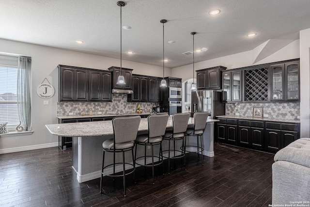 kitchen featuring pendant lighting, appliances with stainless steel finishes, dark hardwood / wood-style flooring, backsplash, and a kitchen island with sink