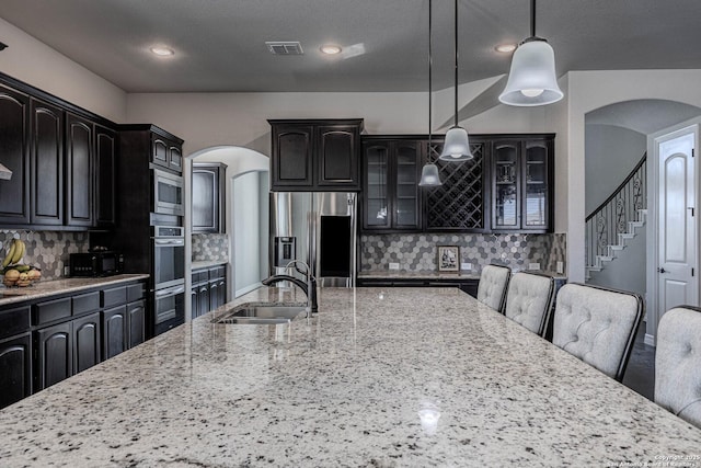 kitchen with appliances with stainless steel finishes, sink, backsplash, hanging light fixtures, and light stone counters