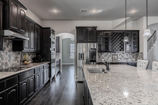 kitchen with light stone countertops, appliances with stainless steel finishes, sink, and decorative light fixtures