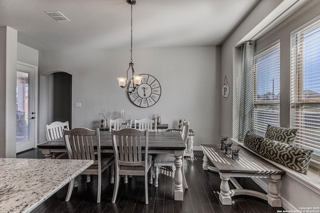 dining room with dark wood-type flooring, plenty of natural light, and an inviting chandelier