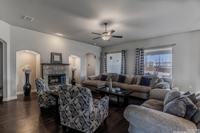 living room featuring dark wood-type flooring, ceiling fan, a textured ceiling, and a stone fireplace