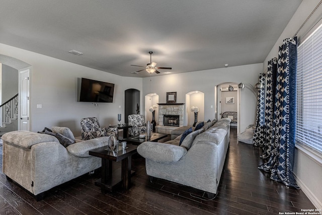 living room featuring ceiling fan, dark hardwood / wood-style flooring, a stone fireplace, and a textured ceiling