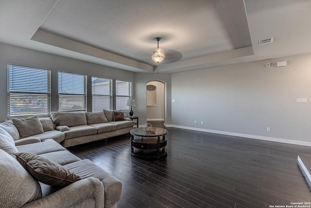 living room featuring ceiling fan, dark wood-type flooring, and a tray ceiling