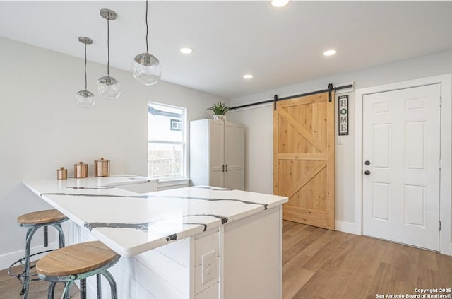 kitchen featuring kitchen peninsula, pendant lighting, a barn door, and light hardwood / wood-style flooring