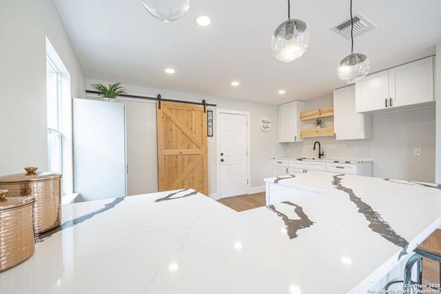 kitchen featuring decorative light fixtures, a barn door, sink, light hardwood / wood-style flooring, and white cabinets