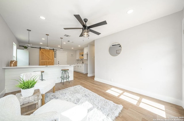 living room featuring ceiling fan, sink, a barn door, and light wood-type flooring