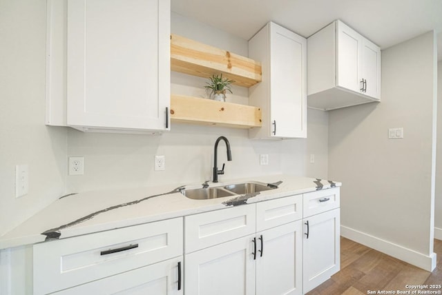 kitchen featuring light stone countertops, white cabinets, and sink