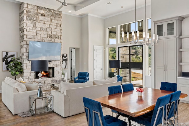 interior space featuring ceiling fan with notable chandelier, a towering ceiling, a stone fireplace, light hardwood / wood-style flooring, and crown molding