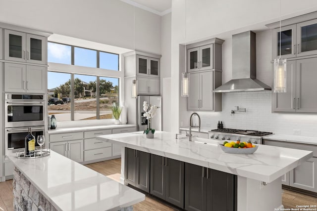 kitchen with stainless steel appliances, a kitchen island with sink, and wall chimney range hood