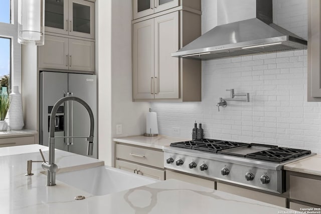 kitchen with decorative backsplash, wall chimney range hood, light stone counters, and stainless steel appliances