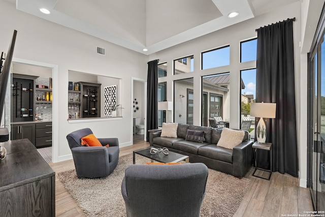 living room featuring a high ceiling, light hardwood / wood-style flooring, and bar area