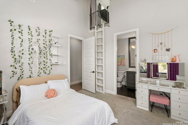 carpeted bedroom with ensuite bathroom and a towering ceiling