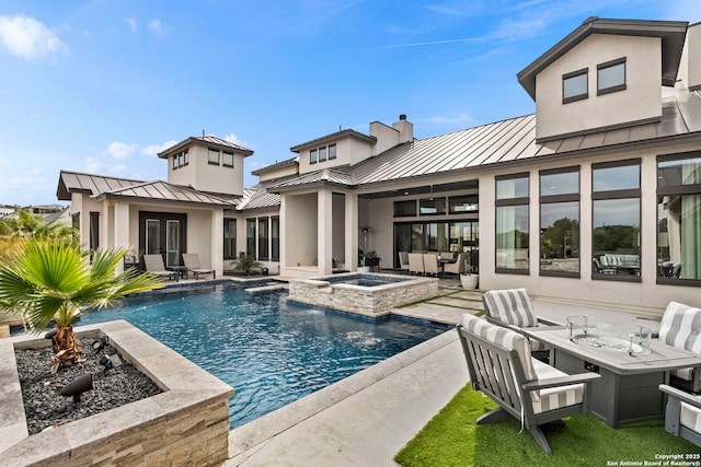 back of house with a swimming pool with hot tub, a patio area, a fire pit, and pool water feature