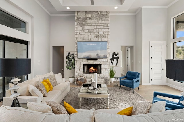 living room featuring a high ceiling, a stone fireplace, ornamental molding, and light hardwood / wood-style floors