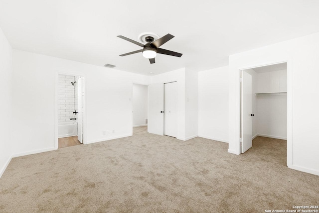 unfurnished bedroom featuring ceiling fan, light colored carpet, a spacious closet, and connected bathroom