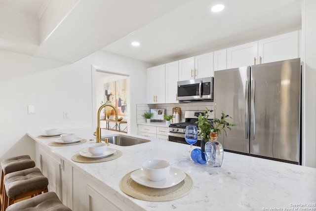 kitchen with white cabinetry, stainless steel appliances, light stone counters, a breakfast bar, and sink