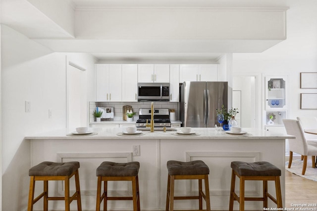 kitchen with kitchen peninsula, stainless steel appliances, white cabinetry, and a breakfast bar