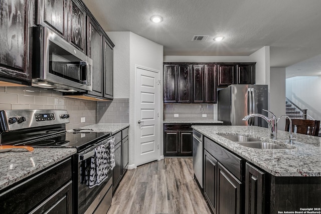 kitchen featuring sink, light hardwood / wood-style flooring, a kitchen island with sink, appliances with stainless steel finishes, and a textured ceiling