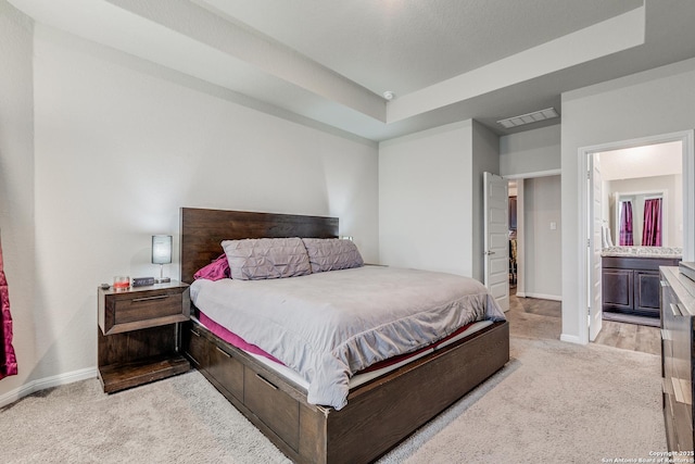 bedroom with ensuite bathroom, light colored carpet, and a tray ceiling