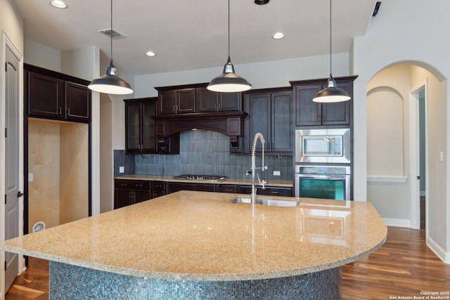 kitchen with pendant lighting, decorative backsplash, sink, a kitchen island with sink, and appliances with stainless steel finishes