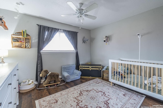 bedroom with ceiling fan, dark hardwood / wood-style flooring, a crib, and a textured ceiling